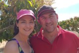 Katrina and Marcello Avolio wearing caps, standing in front of a mango tree